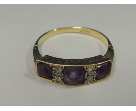 A ladies Edwardian style three stone amethyst ring interspersed by four diamonds in a raised gallery mount on a yellow metal 