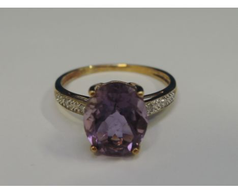 A ladies dress ring having an oval amethyst stone in a raised claw mount with diamond chip decoration to shoulders on a yello