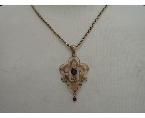 An Edwardian yellow metal pendant stamped 9ct having a central garnet with further drop on a yellow metal chain stamped 9ct