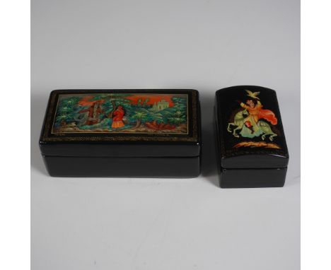 A pair of Soviet-era Russian lacquer boxes, each featuring intricate hand-painted folk art scenes. The larger rectangular box