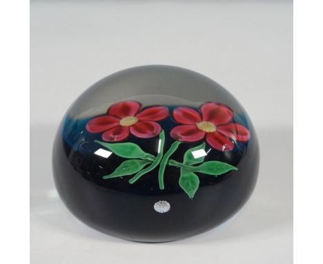 A Baccarat art glass paperweight featuring two vibrant pink lampwork flowers with green stems and leaves, set against a deep 