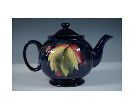 A Moorcroft pottery teapot features a deep cobalt blue ground, accentuated by a bold hand-painted design of cascading leaves 