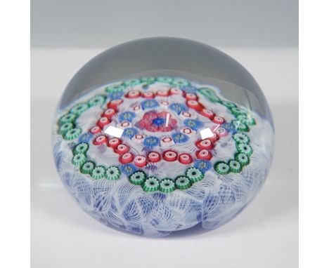 A Baccarat millefiori paperweight featuring a vibrant concentric cane design set atop a delicate white lace cushion, all enca