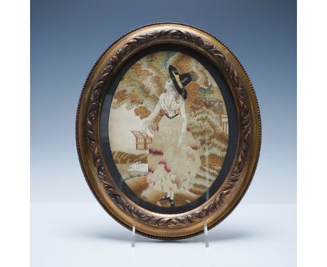 The embroidery features a woman in a dark wide-brimmed hat with beige and red clothing. Her dress is beige with red accents, 