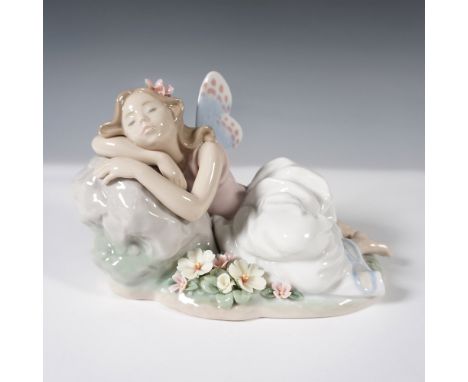 This figurine depicts a delicate fairy resting on a rock amidst a floral landscape, her ethereal wings detailed with soft pas