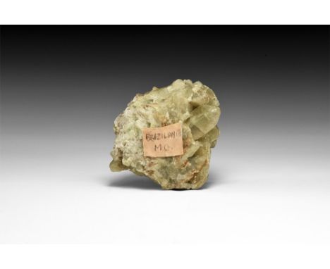 A cluster of greenish-yellow brazilianite crystals from Minas Gerais, Brazil, with old adhesive tape label 'Brazilianite, M.G
