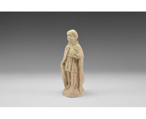 16th century AD.A pipe-clay figurine of one of the three wise men, standing in a long cloak on a domed base, clutching a smal