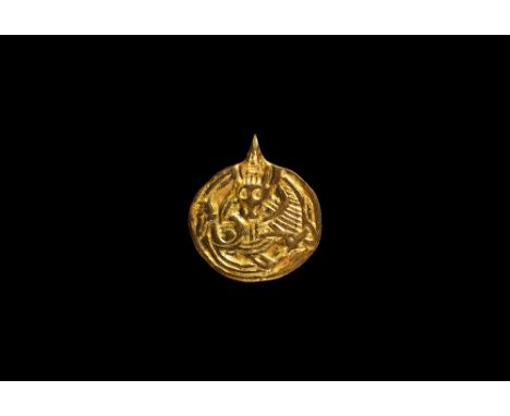 10th century AD.   A silver-gilt discoid pendant with integral loop, banded border with facing male mask on a coiled profile 