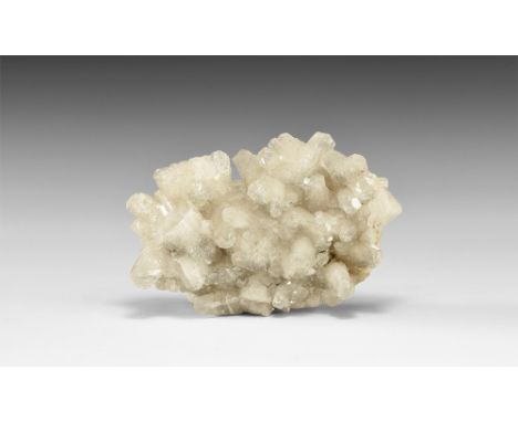 A cluster of barrel-shaped calcite crystals with inclusions of a sulphide mineral; in white card tray with adhesive tape labe