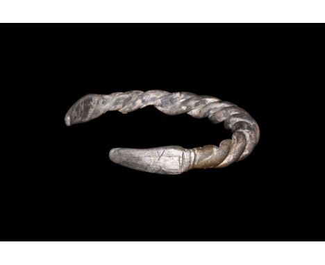 9th-11th century AD.   A round-section silver bracelet with faux-twist detailing to the tapering shank, each finial a tongue-