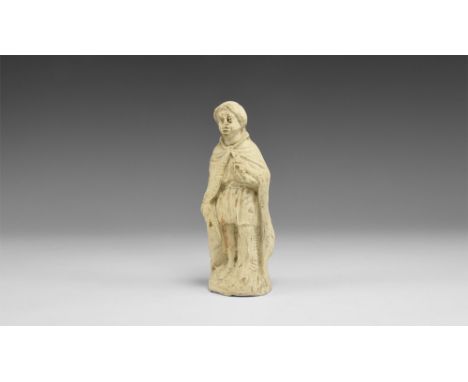 16th century AD.A pipe-clay figurine of one of the three wise men, standing in a long cloak on a domed base, clutching a smal