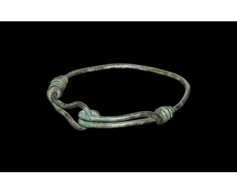2nd millennium BC.A bracelet formed as a bronze rod with one looped finial and recurved to form a hook, each end coiled about