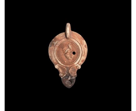 1st century AD.   A hollow-formed terracotta oil lamp with chamfered shoulders, pierced lug handle, volute scrolls above the 