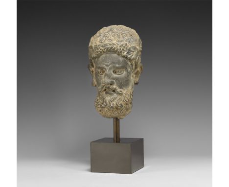 1st-4th century AD.A carved schist head with tight curled hair, wreath to the brow, curled moustache and beard; mounted on a 