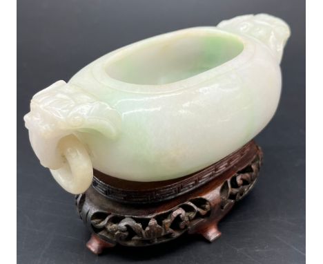 Antique Chinese pale jade small two handle urn vase, together with a later hand carved wooden stand. Vase has carved foo dog 