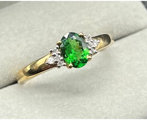 10ct yellow gold ring fitted with an oval cut emerald off set by round cut white topaz stones to the shoulders. [Ring size S]