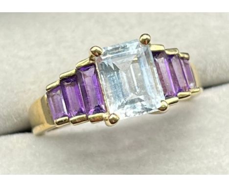 9ct yellow gold ring set with an emerald cut blue aquamarine stone of set by three baguette cut amethyst gem stones to each s