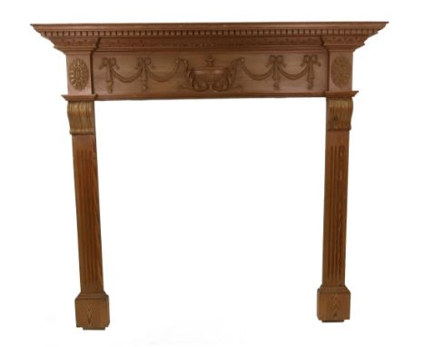 A reproduction George III style waxed pine fire surround, with dentil cornice, carved with a classical urn flanked by ribbon 