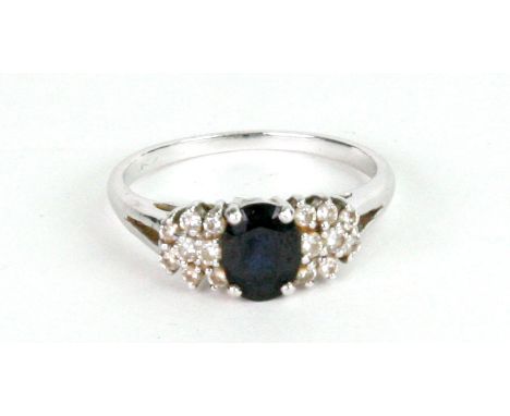 A sapphire and diamond ring, claw-set with the oval mixed-cut sapphire between eight-stone diamond cluster shoulders, stamped