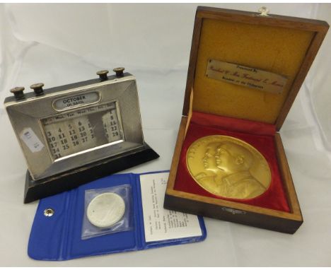 A 1930's engine turned decorated desk calendar, together with a gilded medallion presented by President and Mrs Ferdinand E M