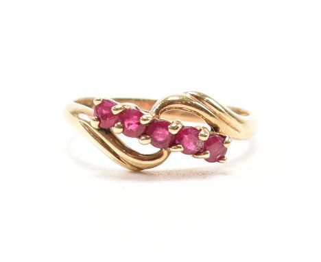 A hallmarked 9ct yellow gold and ruby crossover ring. The ring having five round cut rubies to reeded crossover head and tape