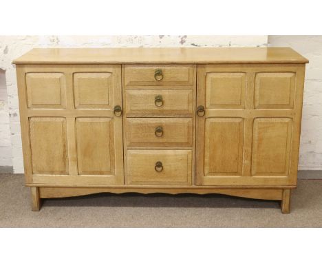 A Cotswold School panelled light oak sideboard with four central drawers flanked by two fitted cupboards.