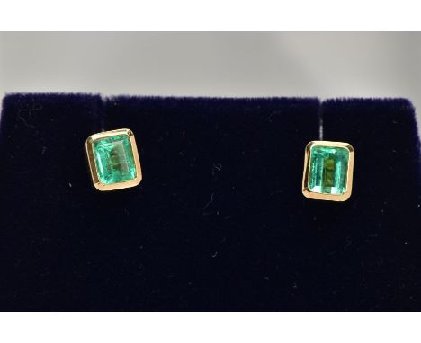 A PAIR OF EMERALD EARRINGS, emerald cut emeralds approximate size 5mm x 4mm, bezel set in a closed back yellow metal setting,