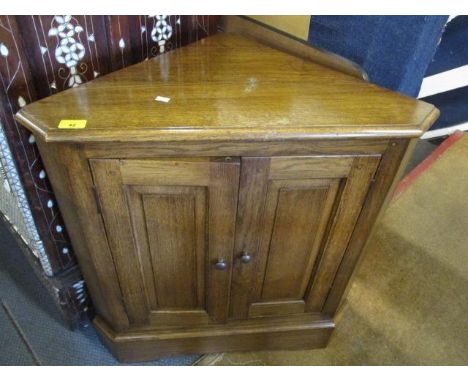 A small reproduction English oak corner cabinet having twin doors revealing a fitted shelf, standing on a plinth base, 30" h 