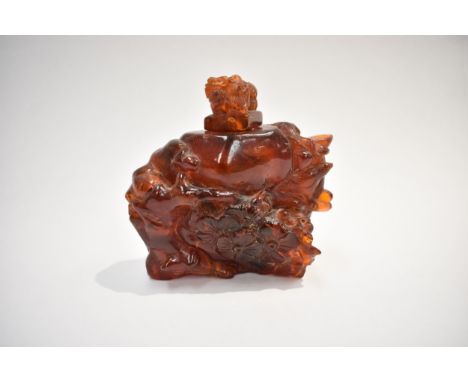 An early 20th Century Chinese amber root carved vessel with figure amongst flowers and a bird, surmounted by dogs of fo, 9cm 
