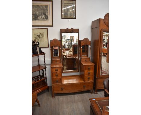 An oak Arts &amp; Crafts wardrobe with twin full length mirrored hanging compartments surmounted by roundels flanking a small