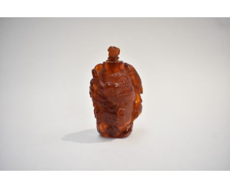 An early 20th Century Chinese carved amber vessel, a figure pointing to a symbol amongst flowers, surmounted by a dog of fo l