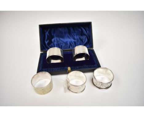 A cased pair of Atkin Brothers silver napkin rings, Sheffield 1908 and three further examples, one with monogram to cartouche