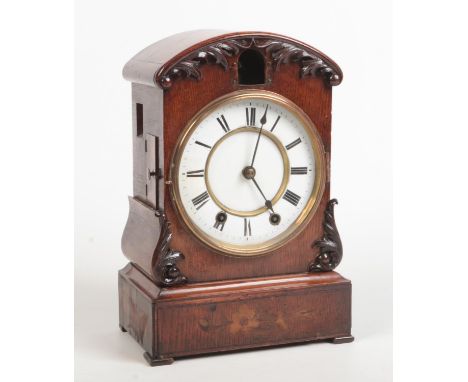 A 19th century German oak cased cuckoo clock. Dome topped, with applied carved scrollwork, white enamel dial and marquetry in