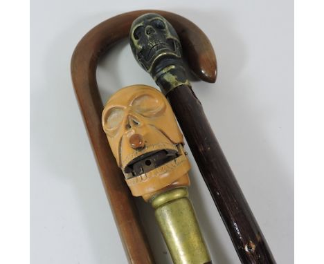 A novelty walking stick, the handle in the form of a money box skull, together with two others 