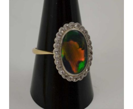 A BLACK OPAL RING, the central oval opal framed by twenty six diamonds, set in platinum on an 18ct gold band, ring size R Con