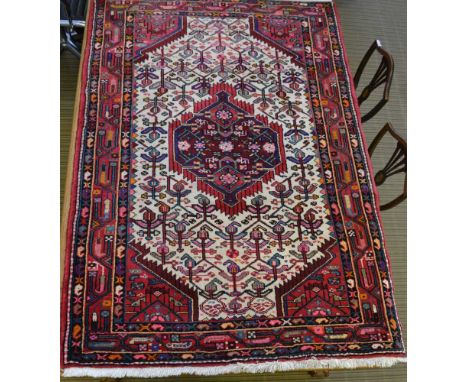 AN IRANIAN WOOL RUG, cream ground, with central stylised floral panel deeply bordered in red, blue, green and pink, 174cm x 1