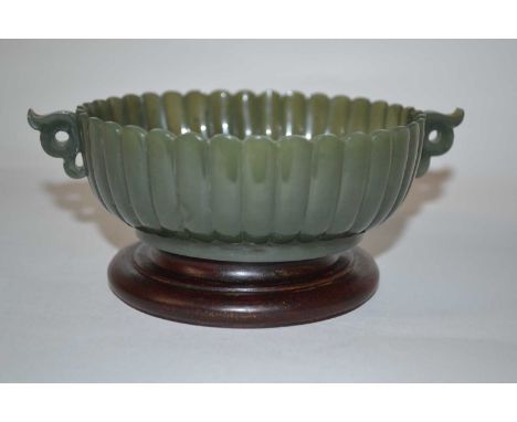A small spinach green jade bowl of fluted form on wooden base, 14cm diameter (handle to handle)