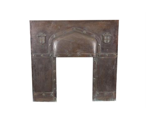 AN ARTS AND CRAFTS BEATEN COPPER FIRE SURROUND, centred with an arched hood and flanked by crested shields and decorated with