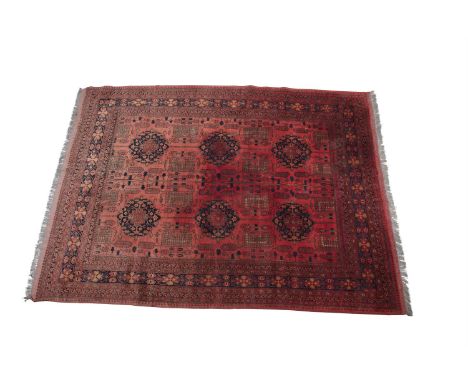 A PERSIAN WOOL RUG, the centre field decorated with two rows, each of three large geometric medallions woven in navy tones, t