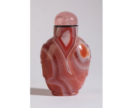 A CHINESE AGATE SNUFF BOTTLE 19th century, with white striations to the red stone, carved mask and ring handles to the should