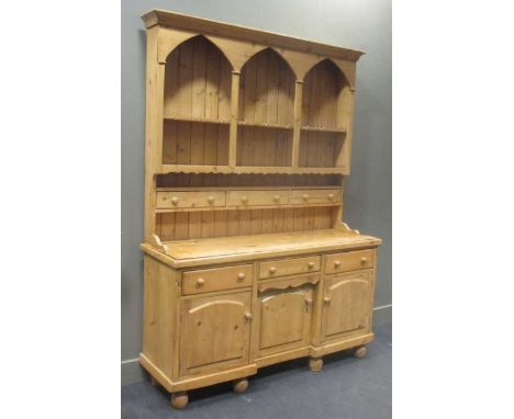 A pine kitchen dresser, the top section with triple arch fronted plate rack above three drawers, the bottom section comprisin