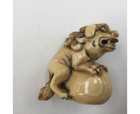 A Japanese Meiji period carved ivory netsuke of Karashishi, the lion dog seated upon a ball, signed to base. Height 3.4 cm.