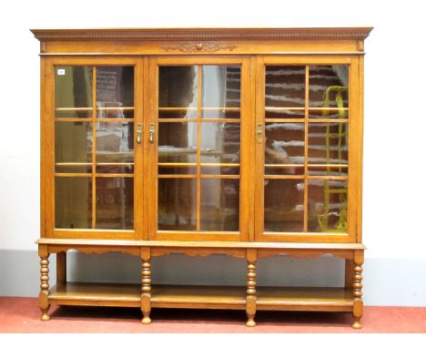 A 1920's Oak Bookcase, the top with moulded edge and dentil cornice to three astragal glazed doors, on bobbin and block suppo