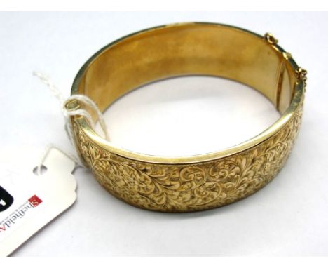 A 9ct Gold Bangle, leaf scroll engraved to the front, hinged to snap clasp.