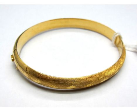A Modern Bangle, textured to the front, hinged to snap clasp stamped "750". 