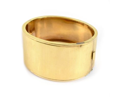 A yellow metal engine turned decorated hinged snap bangle of tapering broad form, internal width 5.6cm, approx 49g.