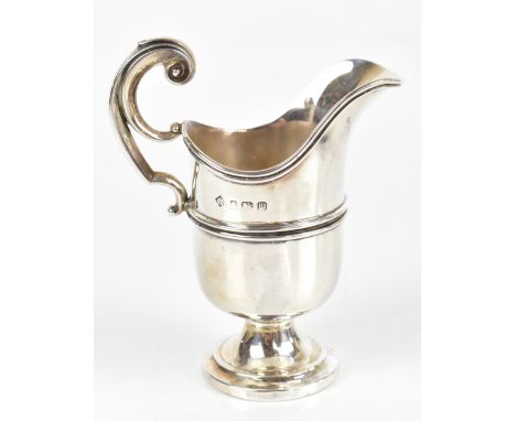 MARTIN HALL &amp; CO; a George V hallmarked silver helmet shaped cream jug, high loop handle and spreading circular foot, Bir