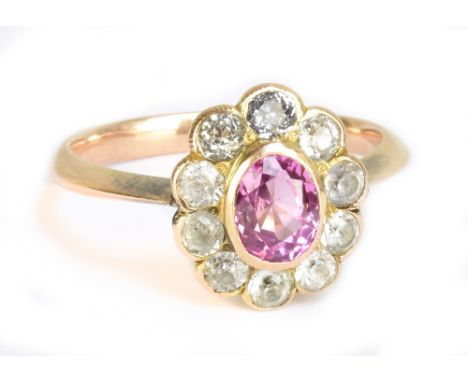 A 1920s yellow metal floral dress ring with outer border of clear stones and central oval pink coloured stone, size M, approx