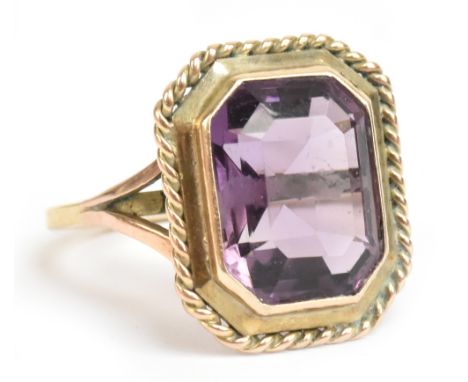 A yellow metal and amethyst dress ring, the faceted rectangular cut stone weighing approx 7.5cts, in a rope twist border, siz