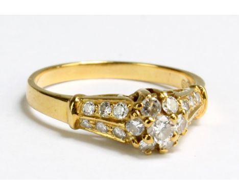 An 18ct yellow gold and diamond daisy cluster ring, the round cut stones in high claw setting flanked by twelve graduated mel